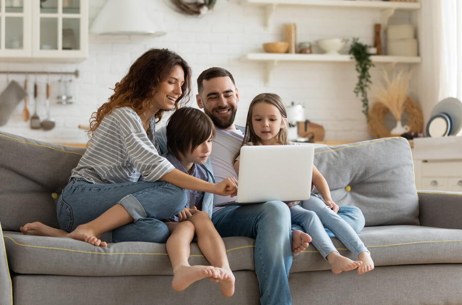 A family of 4 sat on a sofa smiling on a laptop - ordered their Stowable storage.